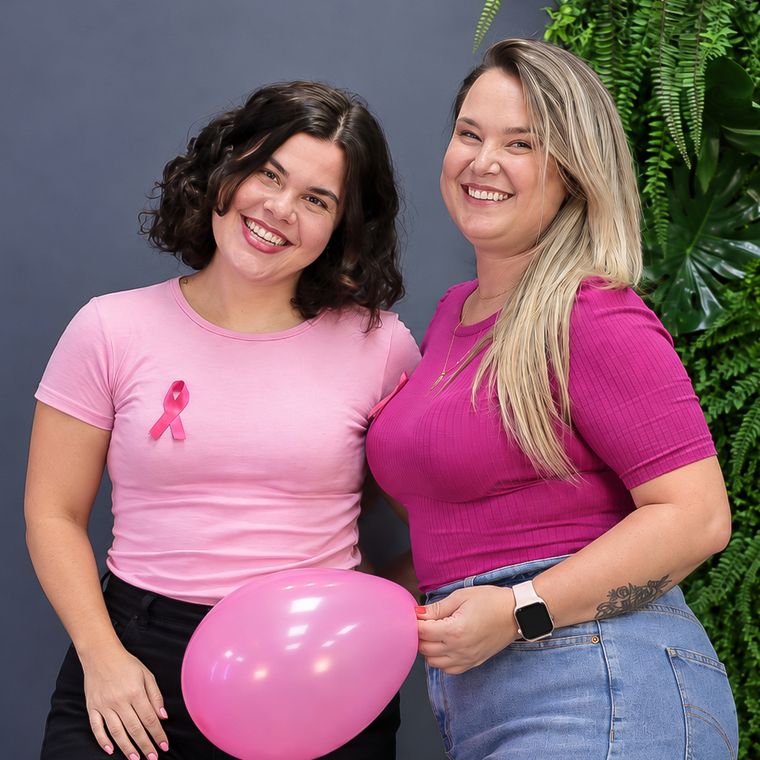Duas profissionais da YouRH com camisetas rosa e laço do Outubro Rosa